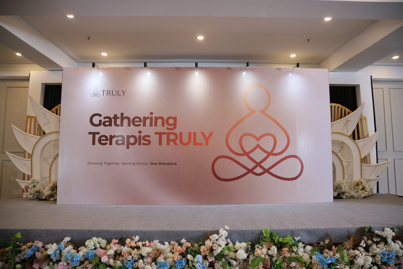 Panggung utama Gathering Terapis TRULY dengan backdrop bertuliskan Growing Together, Serving Better, One Standard